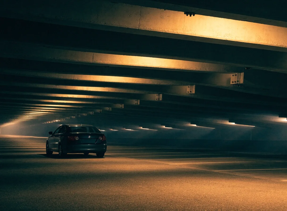 Covered airport car park lane lit by warm ceiling lights at night